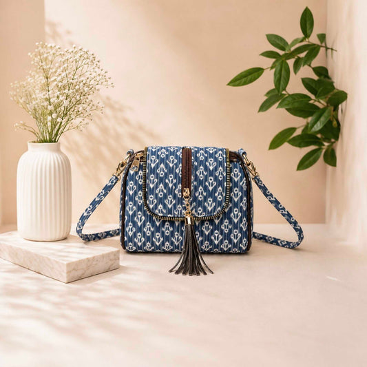 Blue patterned handbag with tassels on a light surface with a vase and plant in the background