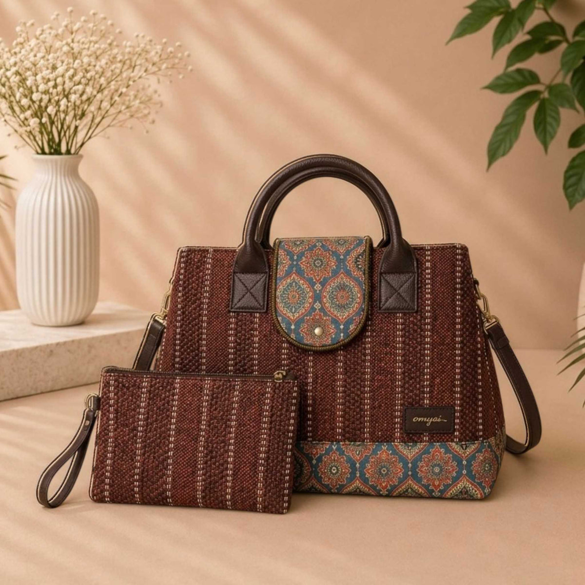 Patterned handbag and pouch set on a beige surface with a vase and plant in the background