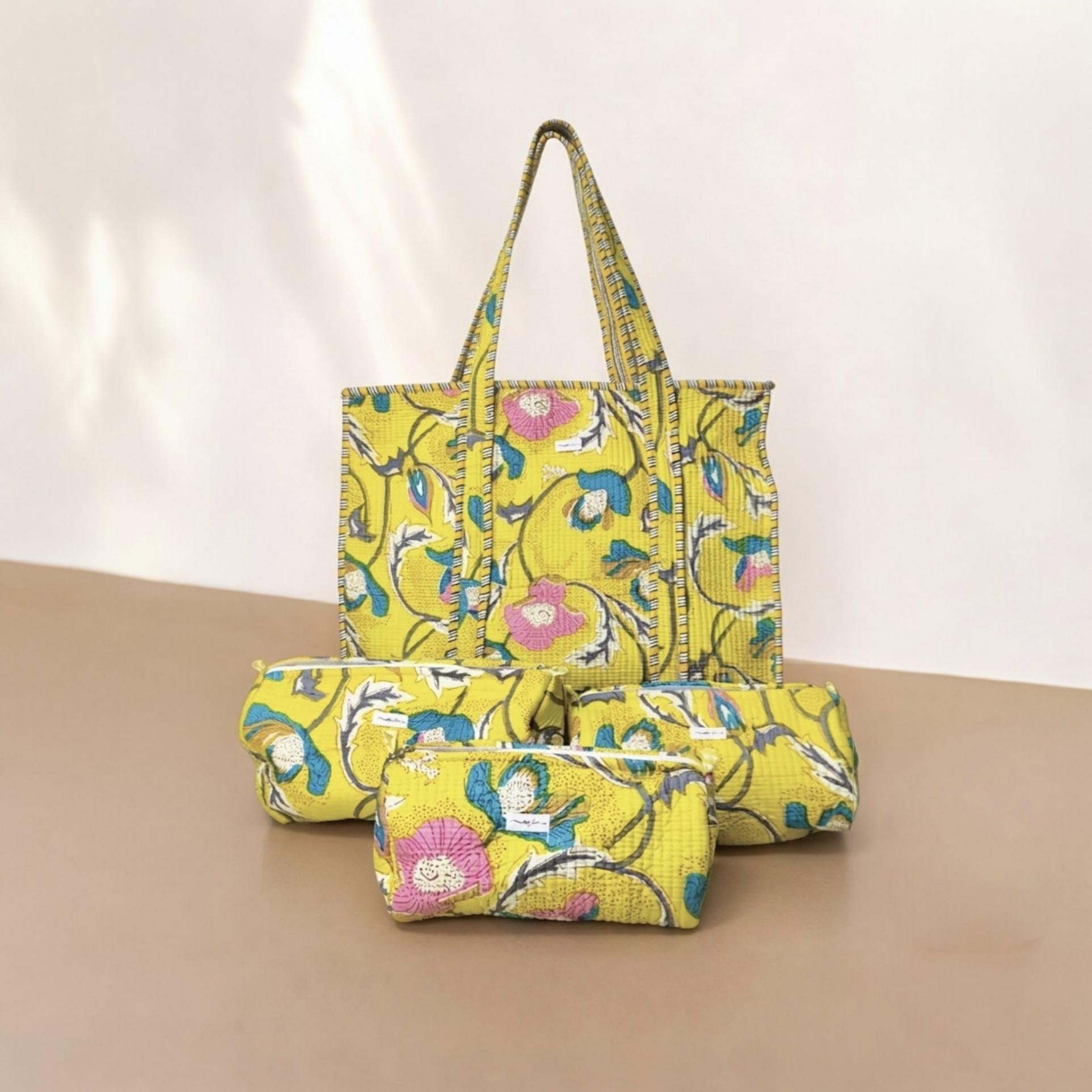 Yellow floral-patterned tote bag and pouch on a beige surface with a light pink background
