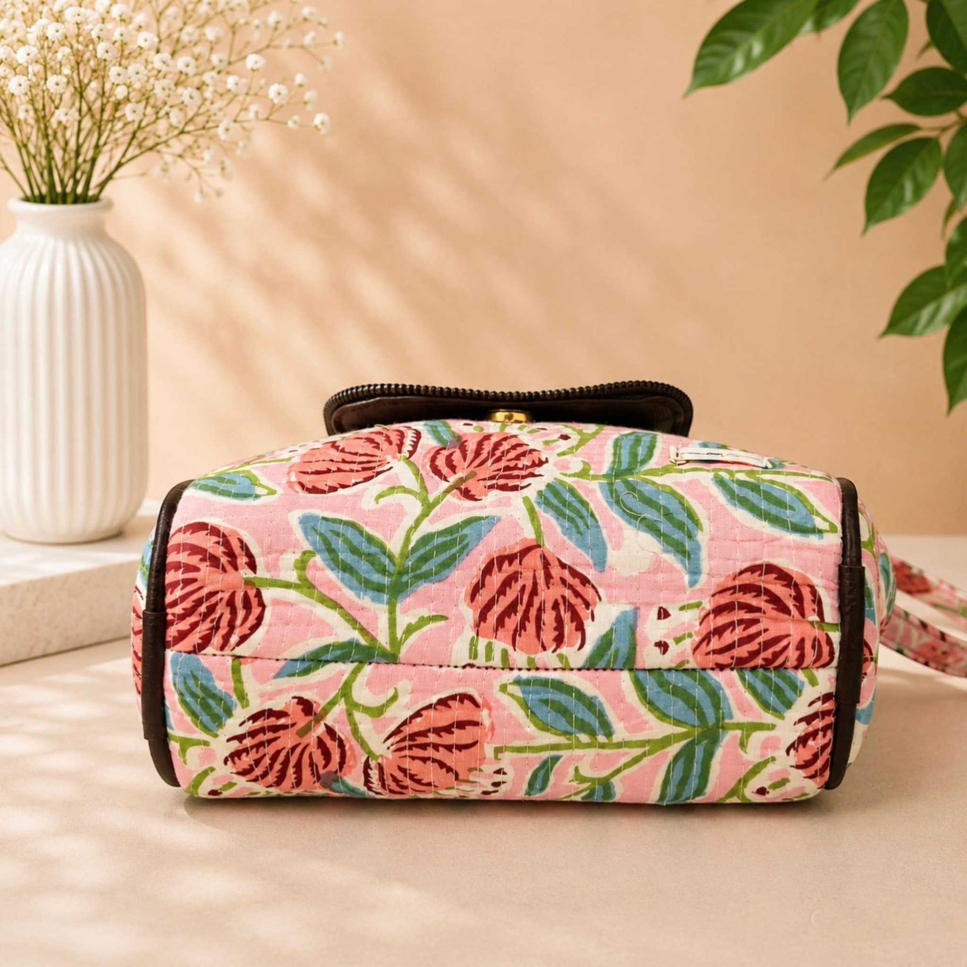 Floral-patterned bag on a beige surface with a vase and plant in the background