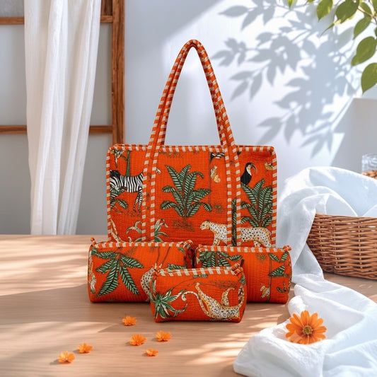 A coordinated orange fabric accessory set on a wooden table, including a tote bag, two zip pouches, and a small wallet, all printed with tropical and safari motifs like zebra, toucan, leopard, and palm leaves. White draped fabric, a wicker basket, and leaf shadows are visible in the background.