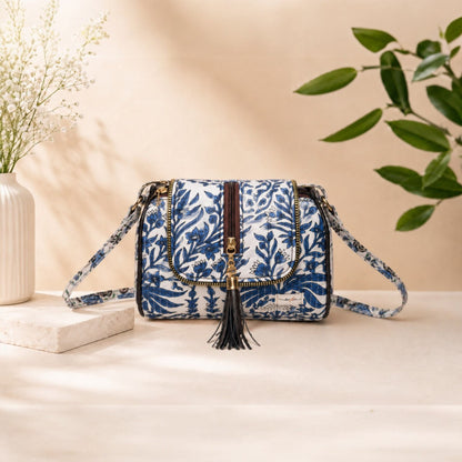 Blue floral patterned handbag with tassel on a beige surface with a plant in the background