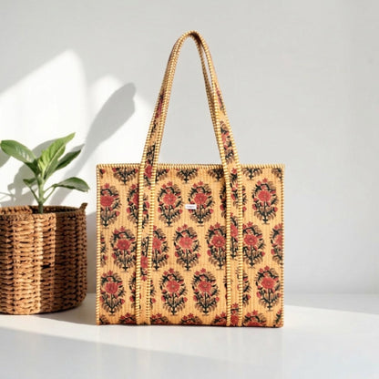 Woven tote bag with floral pattern next to a plant on a light surface.
