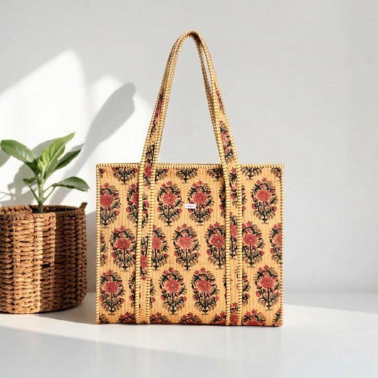 Woven tote bag with floral pattern next to a plant on a light surface.