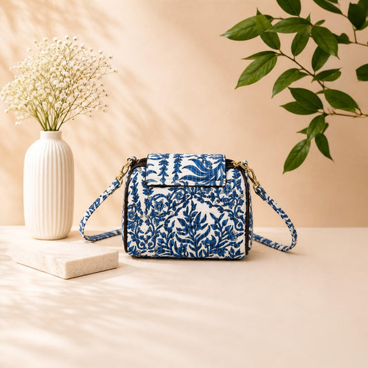 Blue floral patterned handbag on a beige surface with a vase and plant in the background