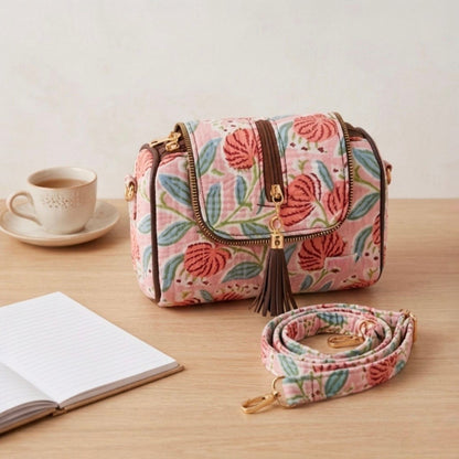 Floral patterned handbag with a matching strap on a wooden surface with a cup and book.