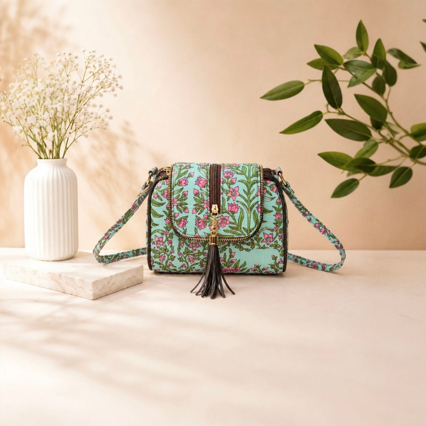 Floral patterned handbag with tassel on a beige surface with a vase and plant in the background