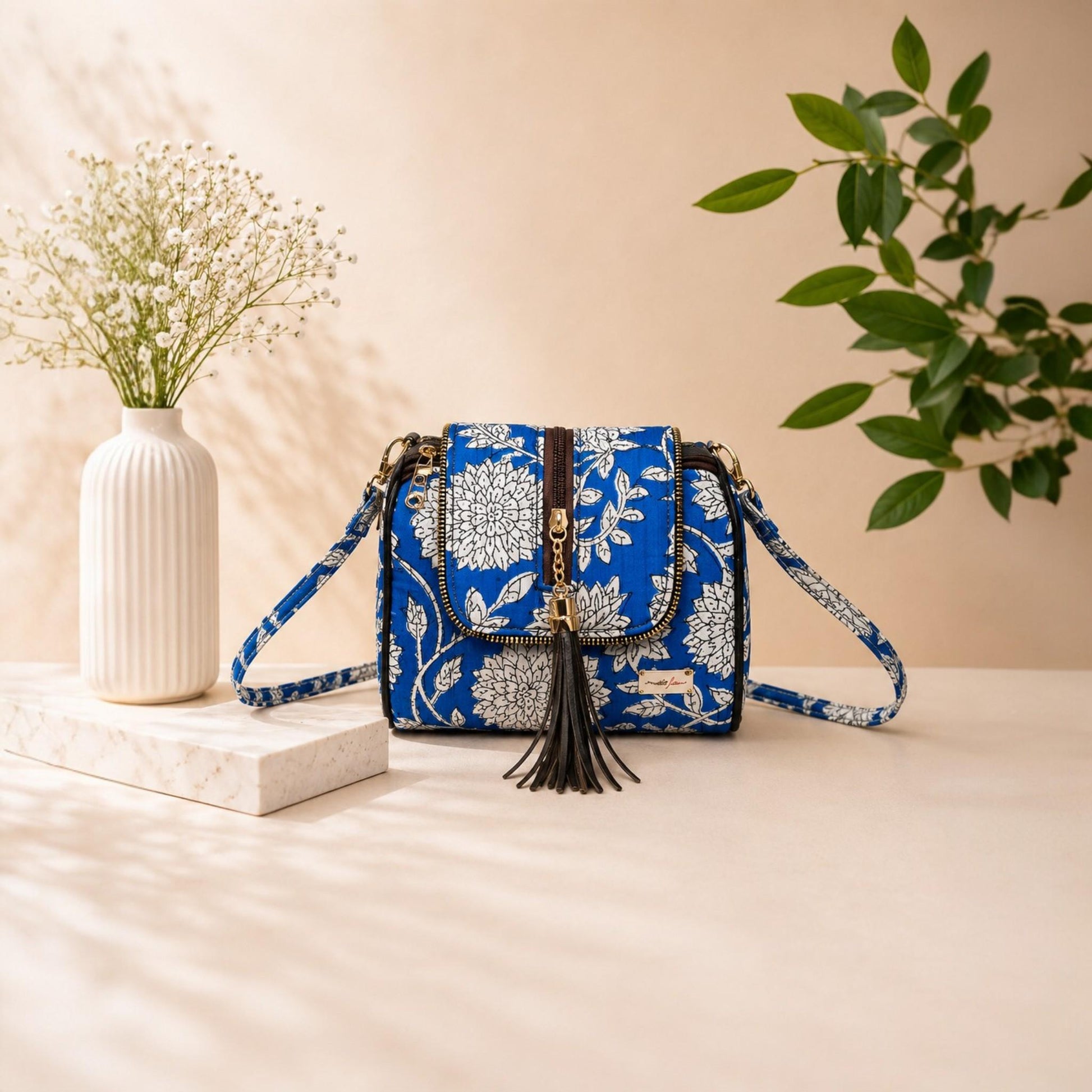 Blue floral patterned handbag with tassel on a beige surface with decorative elements.