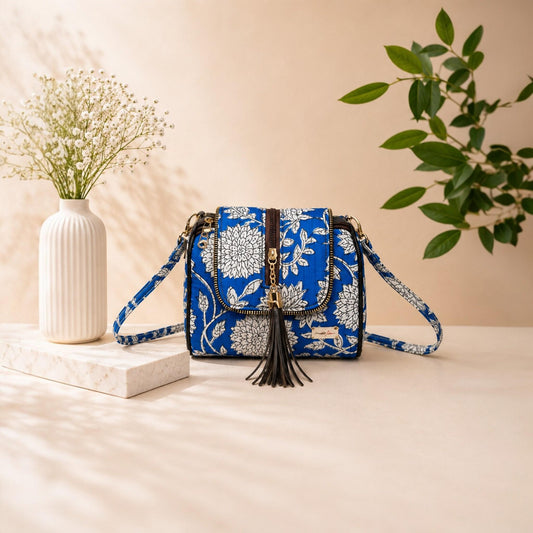 Blue floral patterned handbag with tassel on a beige surface with decorative elements.