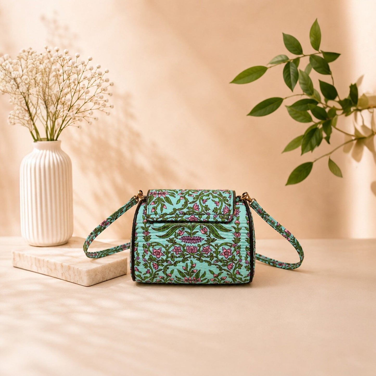 Floral patterned handbag on a beige surface with a vase and plant in the background