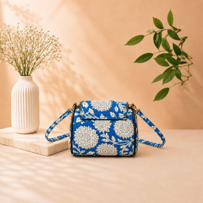 Blue floral-patterned handbag on a beige surface with a vase and plant in the background