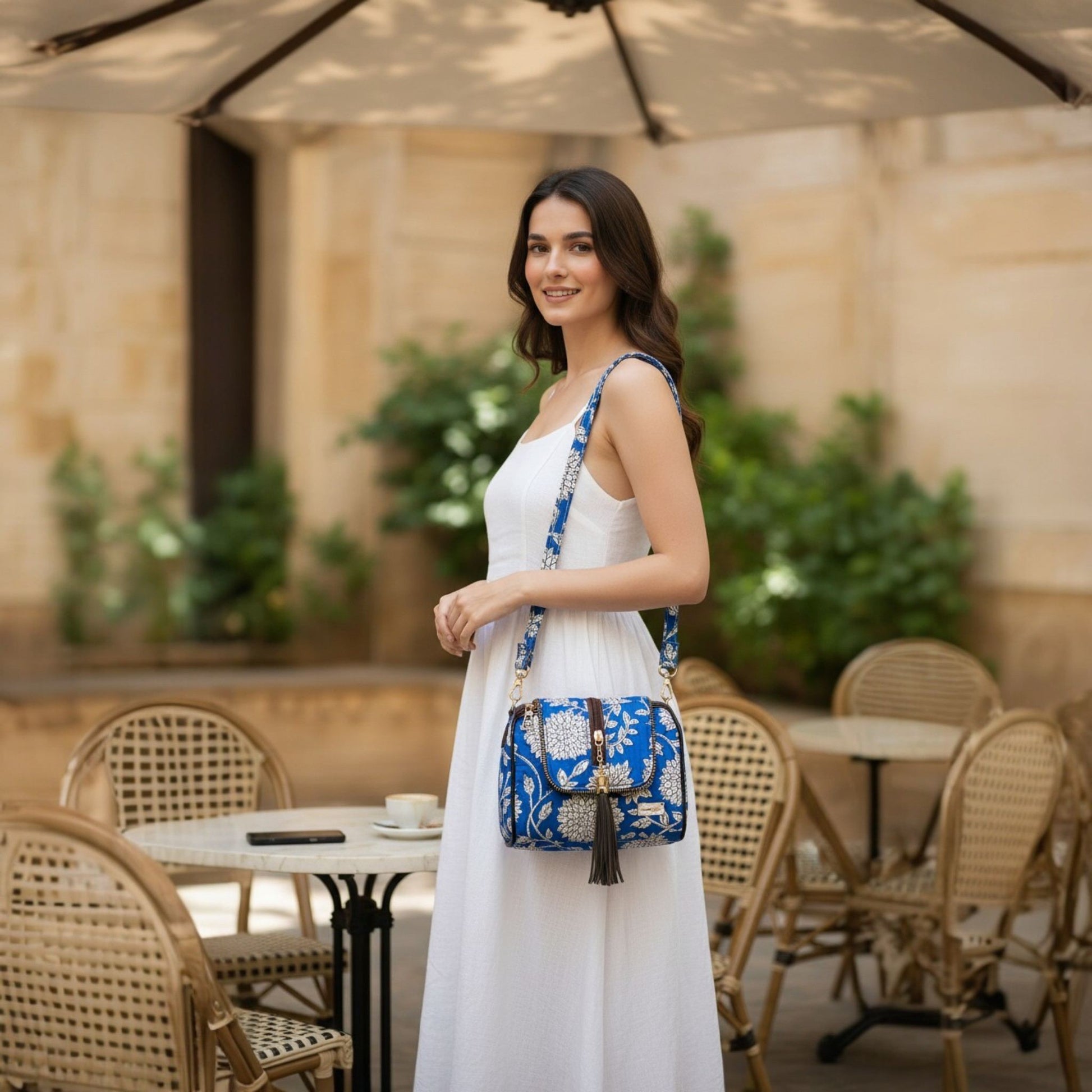 Woman in a white dress holding a blue handbag in an outdoor cafe setting