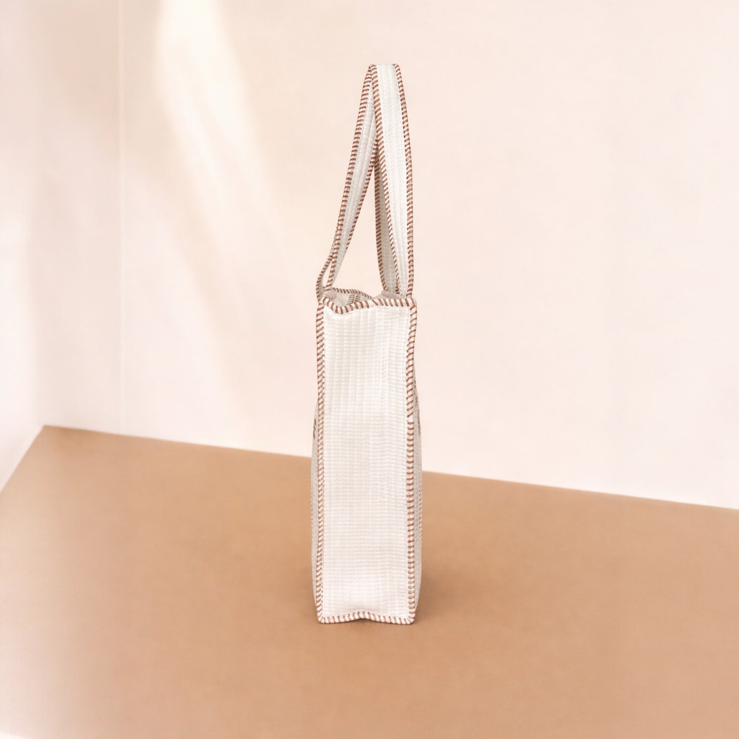 White woven bag with brown trim on a beige surface