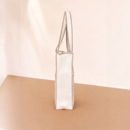 White woven bag with brown trim on a beige surface