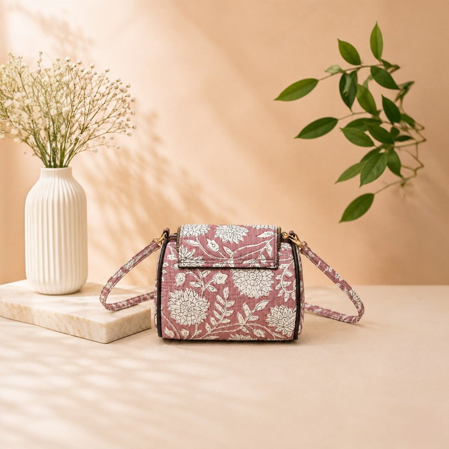 Floral patterned handbag on a wooden surface with a vase and plant in the background