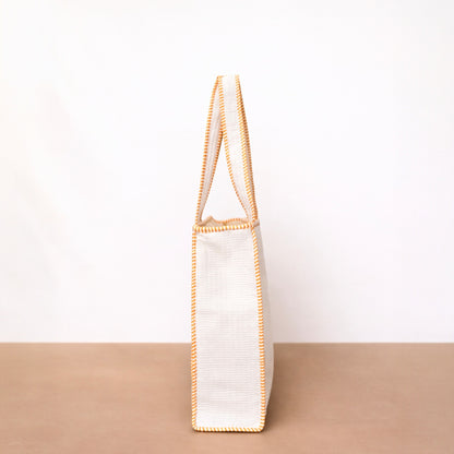 White tote bag with gold trim on a beige surface and white background
