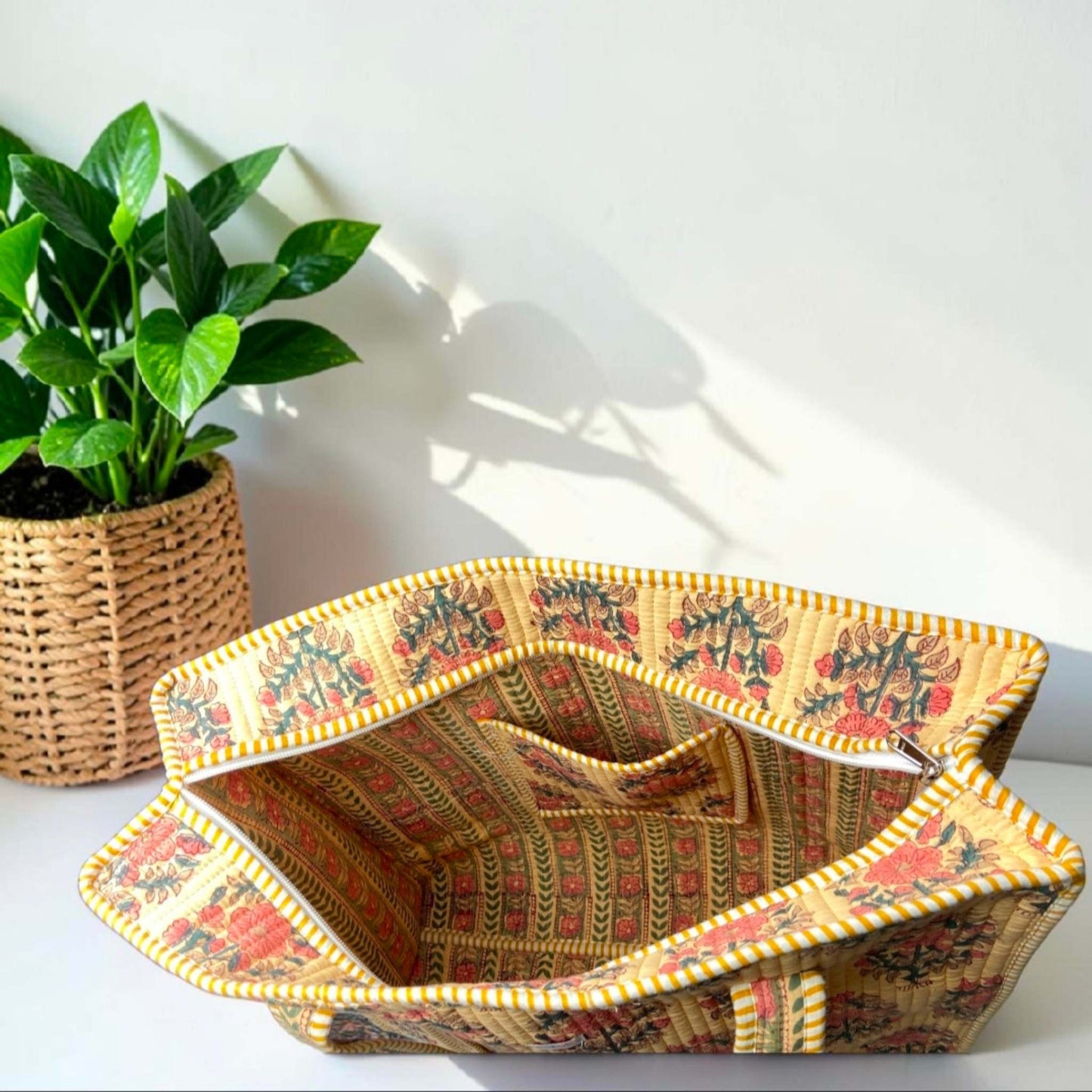 Decorative woven basket with floral patterns on a white surface with a plant in the background.