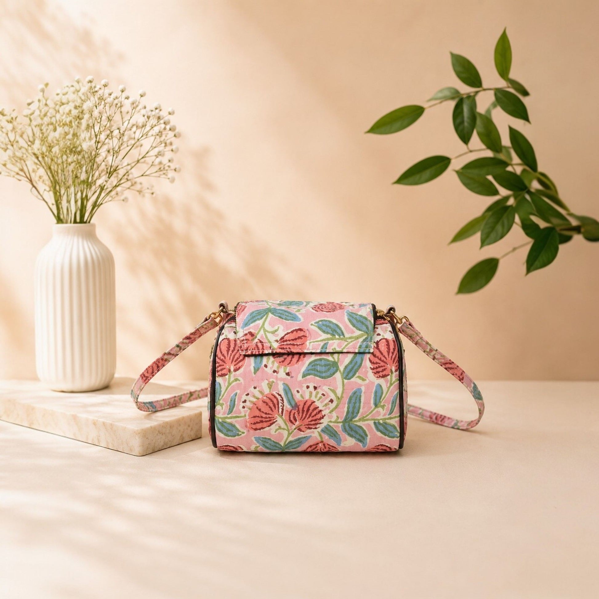 Floral patterned handbag on a beige surface with a vase and plant in the background