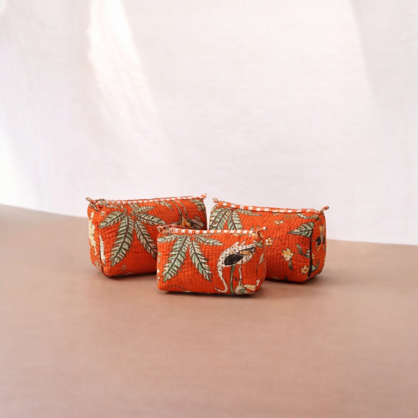 Three orange fabric pouches with animal prints on a beige surface.