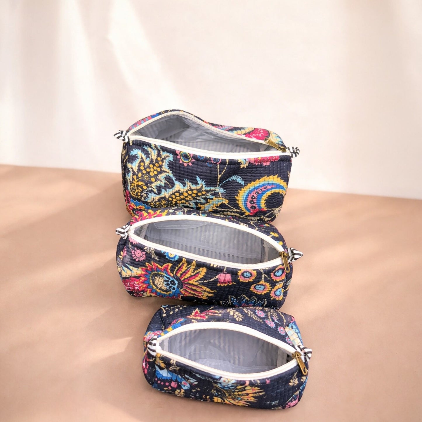 Set of three floral-patterned makeup bags on a beige surface