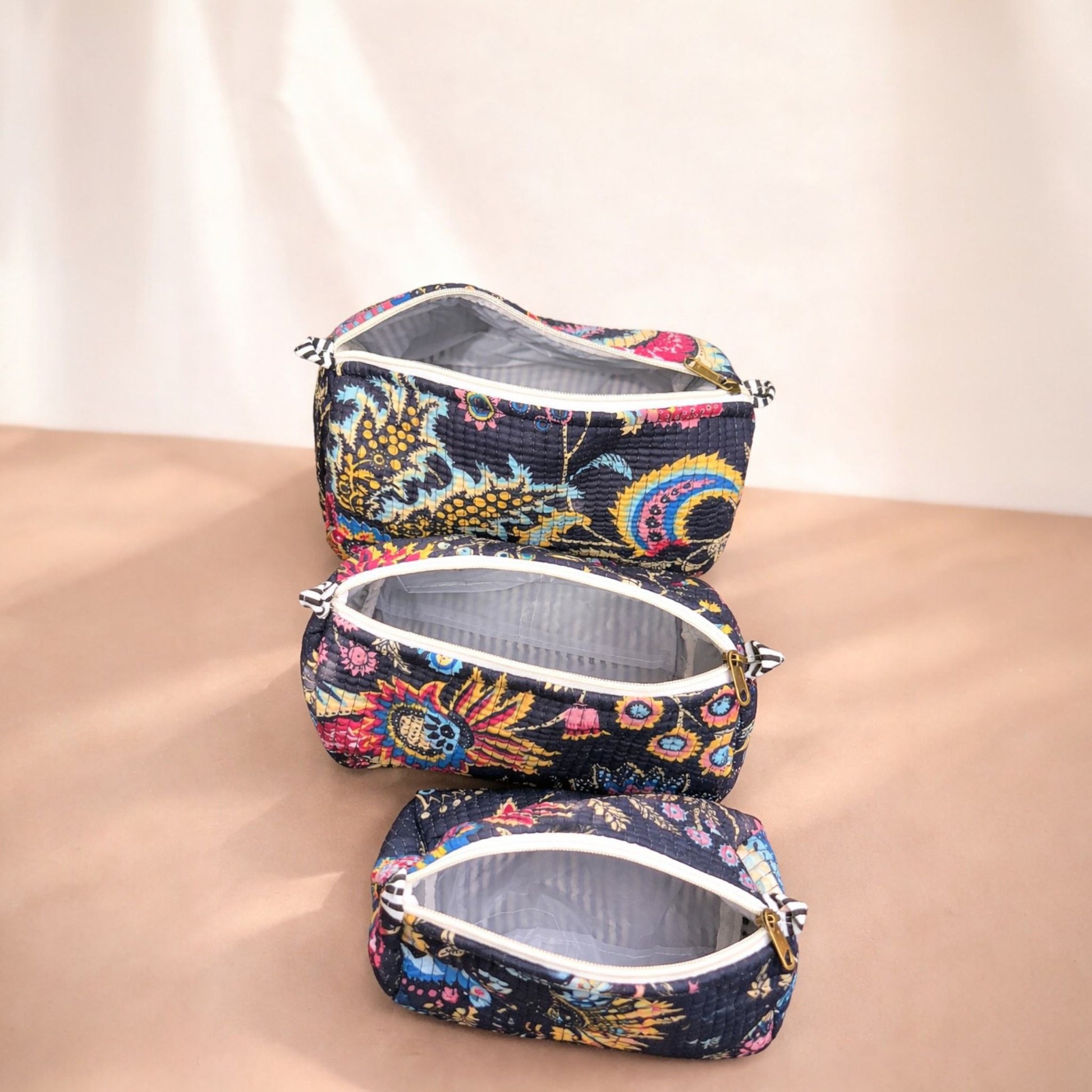 Set of three floral-patterned makeup bags on a beige surface