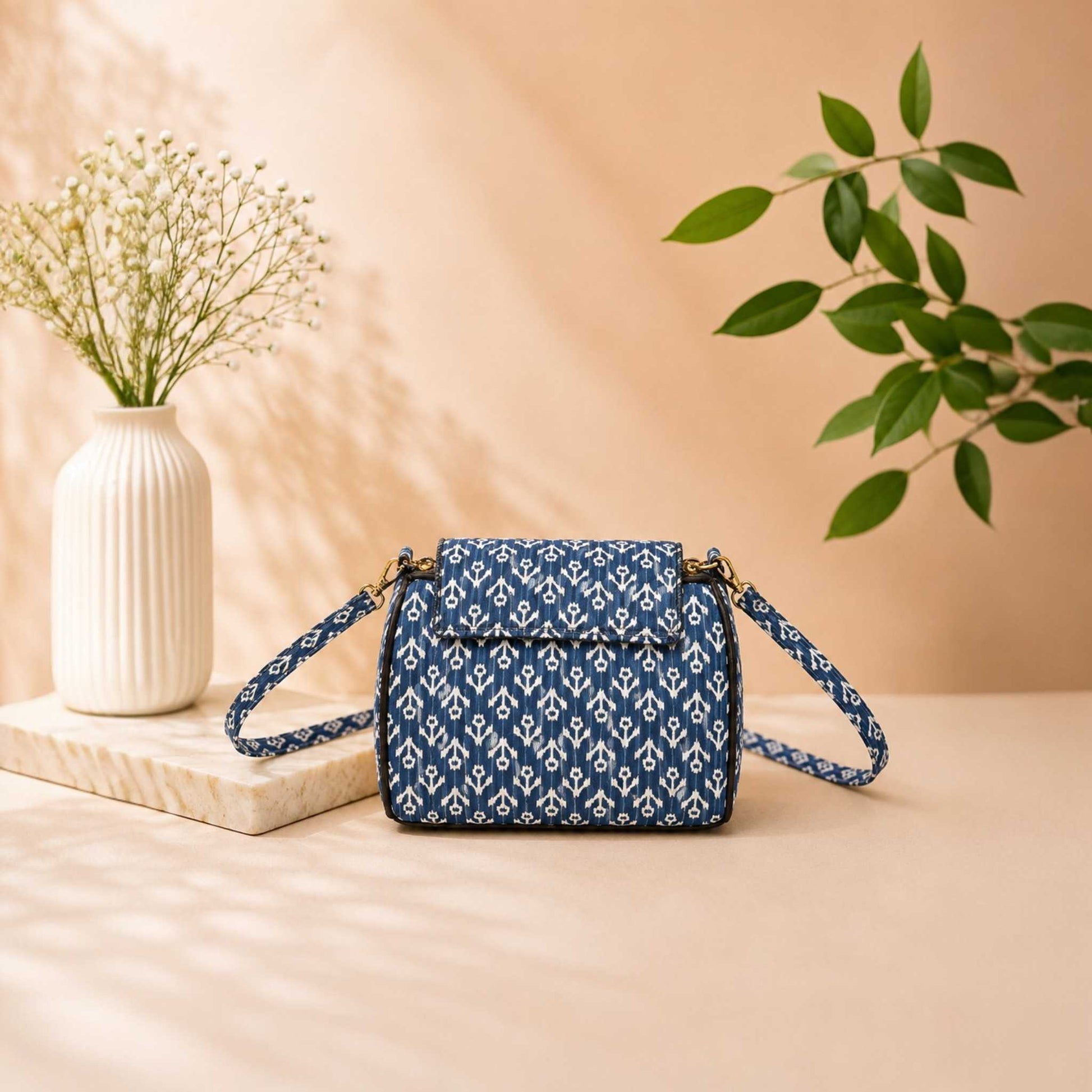 Blue patterned handbag on a beige surface with a vase and plant in the background