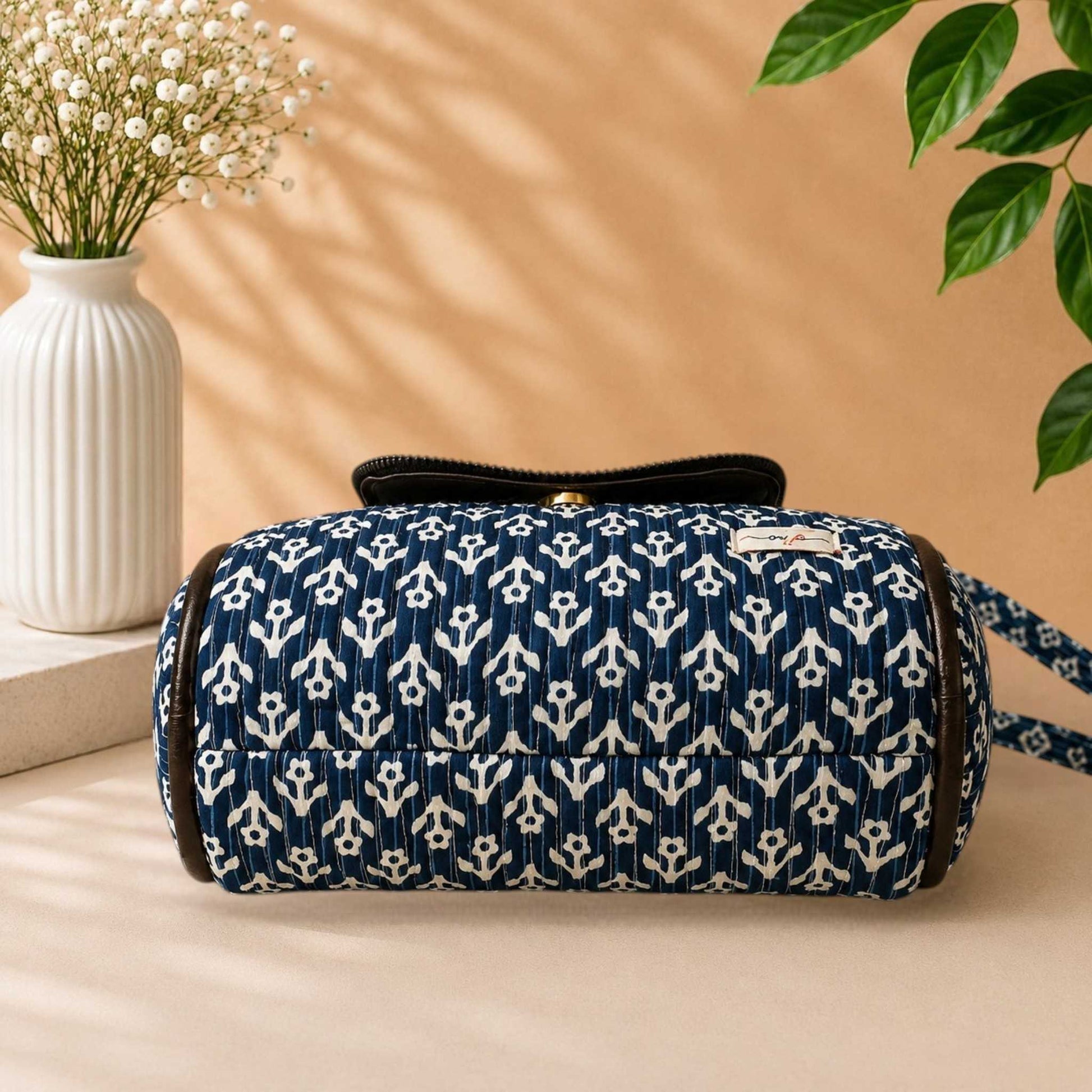 Blue and white patterned bag on a beige surface with a vase and plant in the background