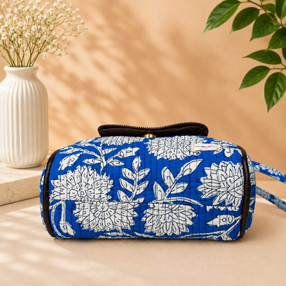 Blue floral-patterned bag on a beige surface with a vase and plant in the background