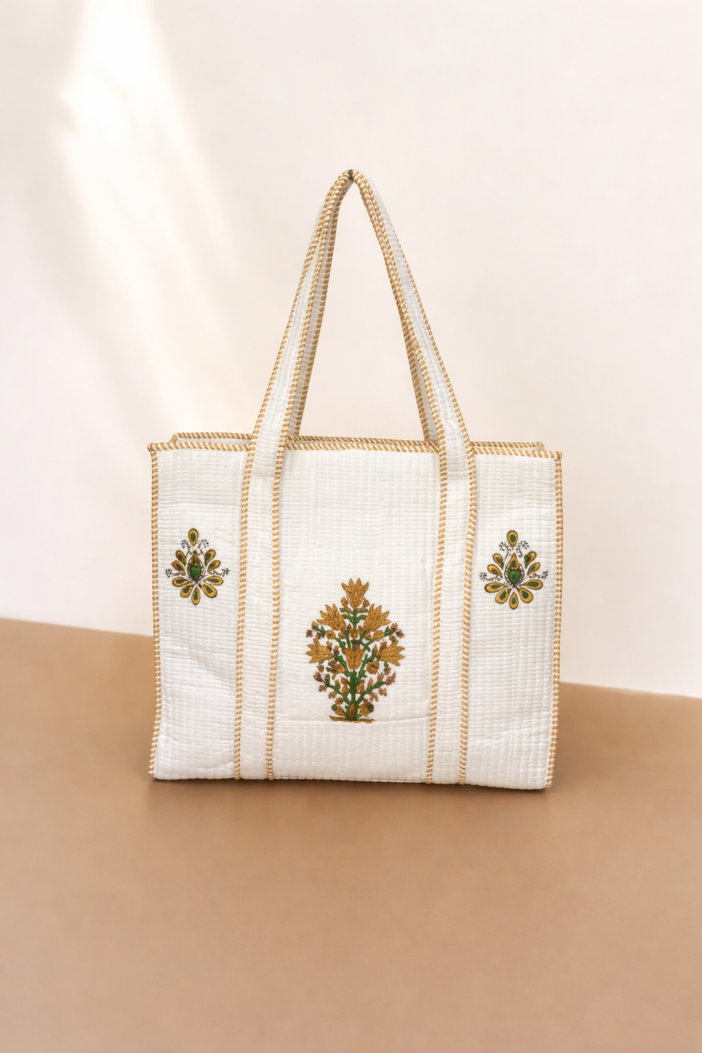 White tote bag with gold embroidery on a beige background