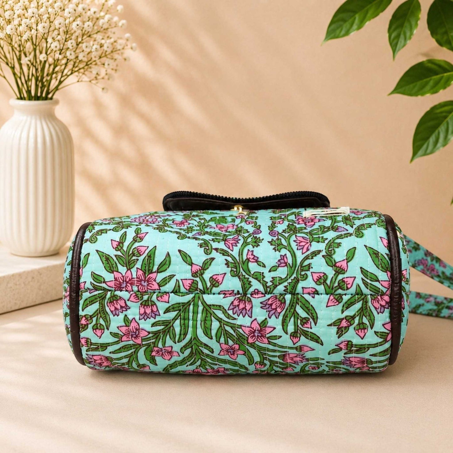 Floral-patterned cylindrical bag on a beige surface with a vase and plant in the background