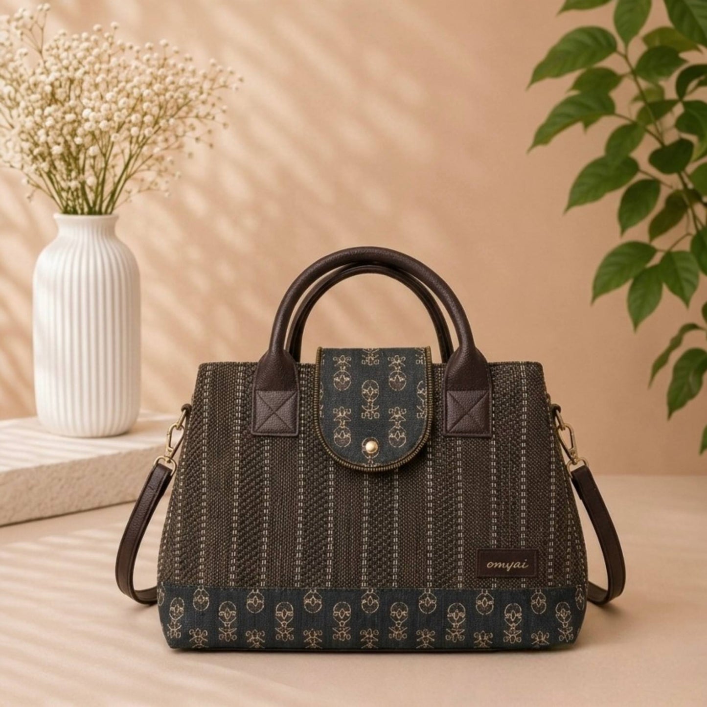 Black textured handbag with skull pattern on a beige surface with a vase and plant in the background