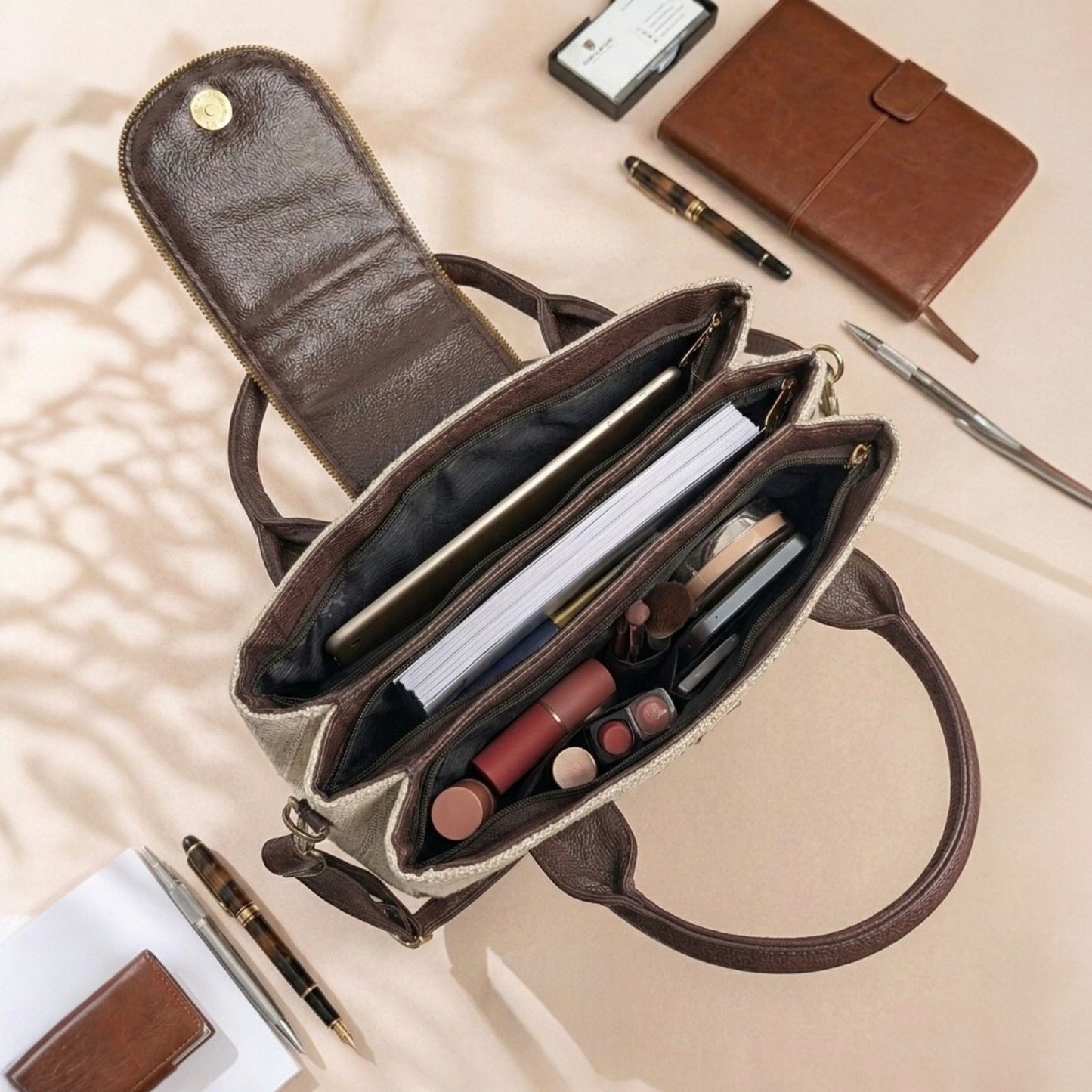 Open brown handbag with makeup items on a beige surface