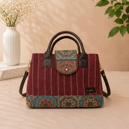 Red patterned handbag with black handles on a beige surface, with a vase and plant in the background.