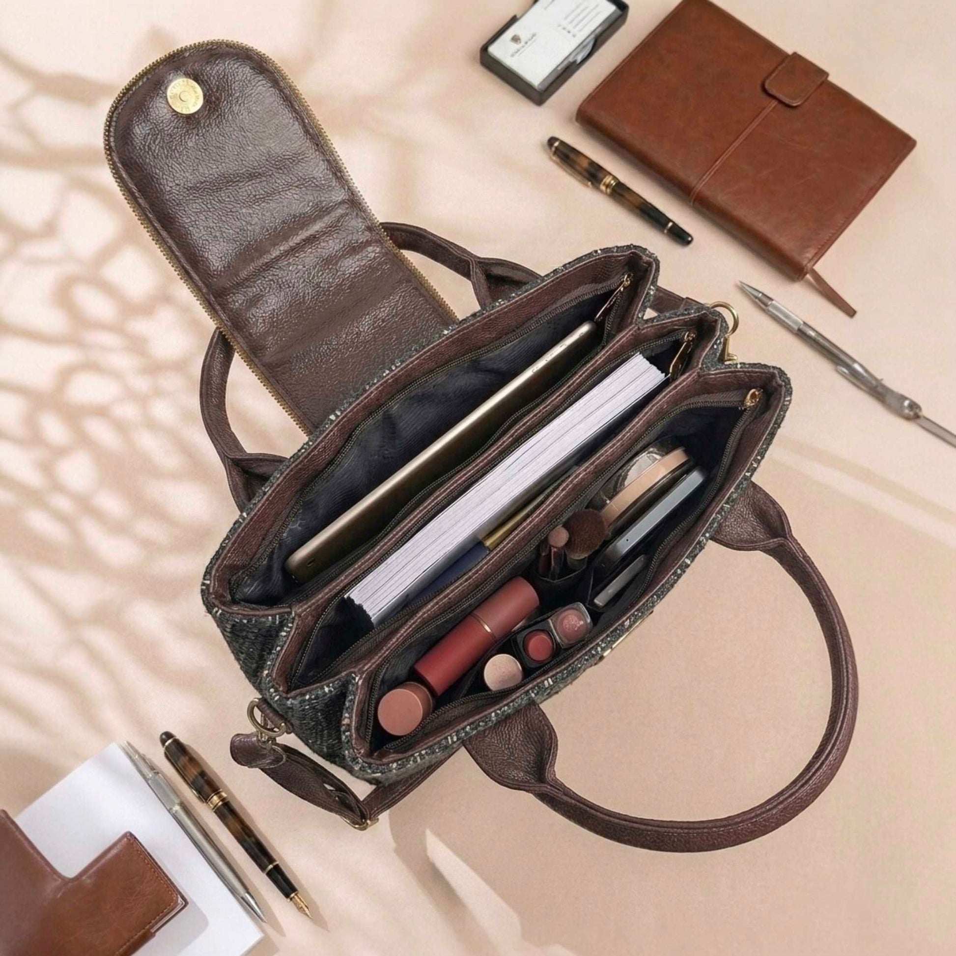 Open brown handbag with makeup and stationery items on a beige surface