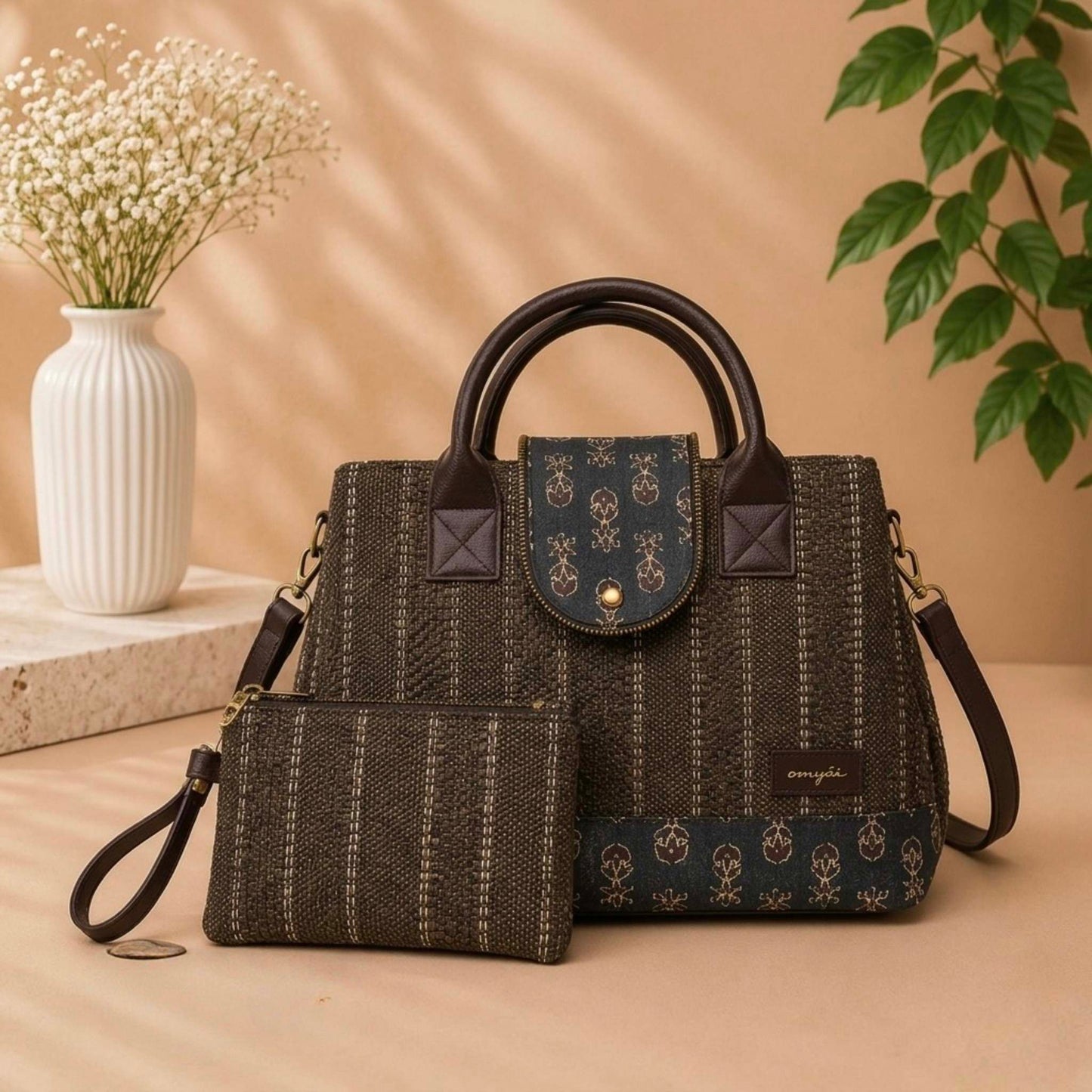 Dark textured handbag with matching pouch on a beige surface, with a vase and plant in the background.