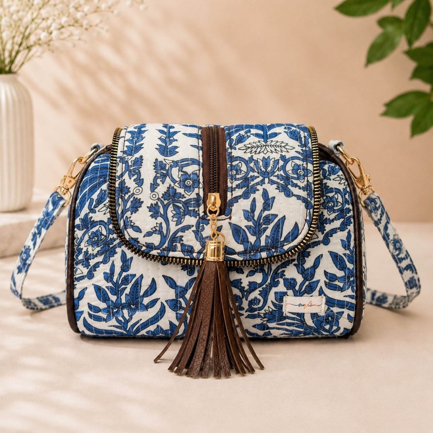 Blue floral patterned handbag with a tassel on a beige surface